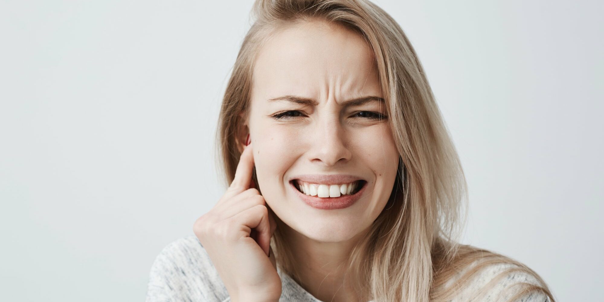 probleme-mit-ohren.jpg Junge Frau mit schmerzverzerrtem Gesicht, hält sich den rechten Ohrbereich mit der Hand.