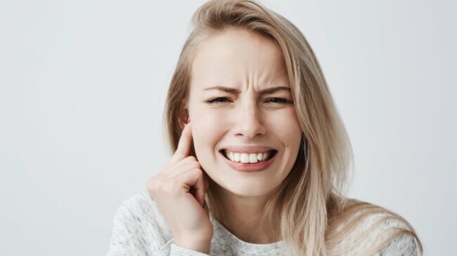 probleme-mit-ohren.jpg Junge Frau mit schmerzverzerrtem Gesicht, hält sich den rechten Ohrbereich mit der Hand.