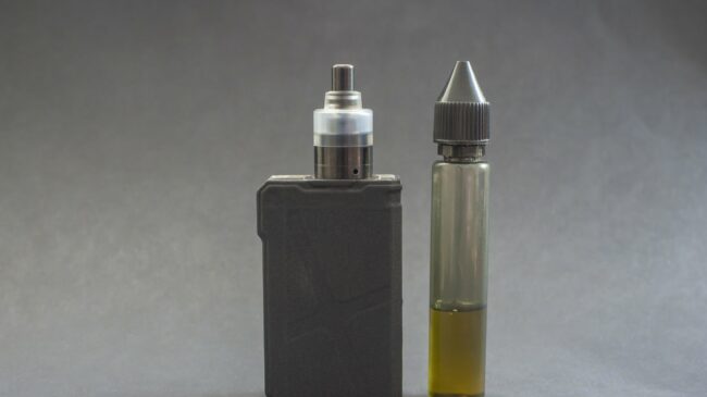 Ein Verdampfergerät links, daneben eine Flasche mit E-Liquid in einer transparenten Verpackung.