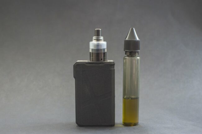 Ein Verdampfergerät links, daneben eine Flasche mit E-Liquid in einer transparenten Verpackung.