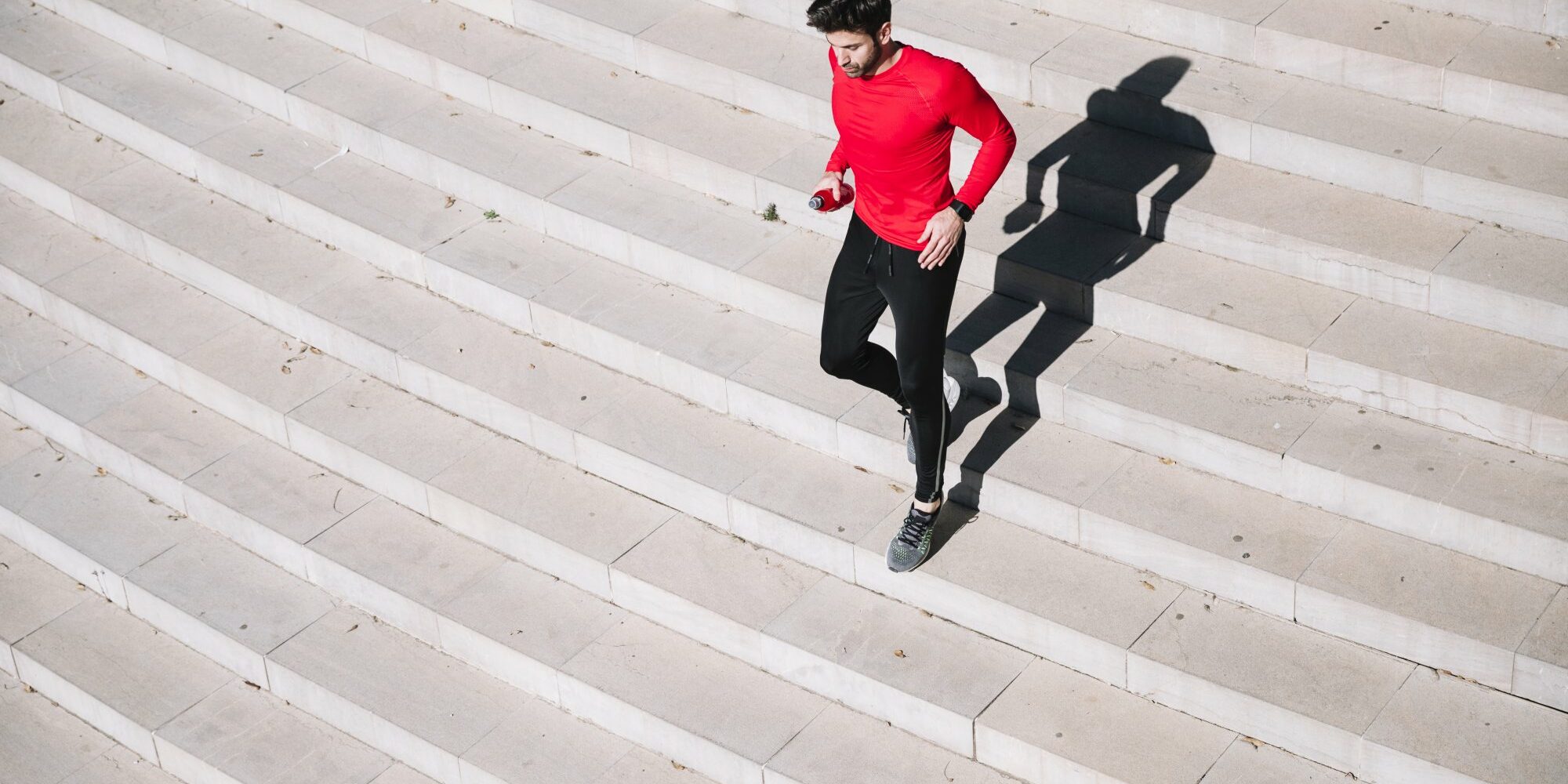 Mann in rotem Shirt joggt über eine helle Treppe, sein Schatten ist deutlich sichtbar.