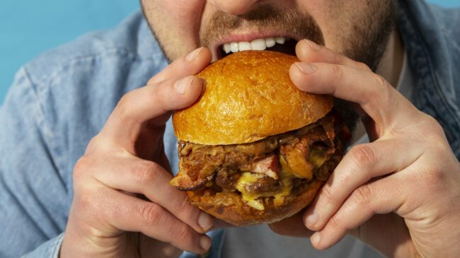 Tierische_Fette__1_.jpg Eine Person hält einen saftigen Burger mit einem goldenen Brötchen und beabsichtigt, ihn zu essen.