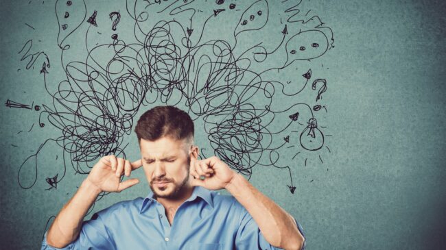 Ein Mann in einem blauen Hemd hält sich die Ohren zu, während verworrene Gedanken und Symbole über seinem Kopf schweben.