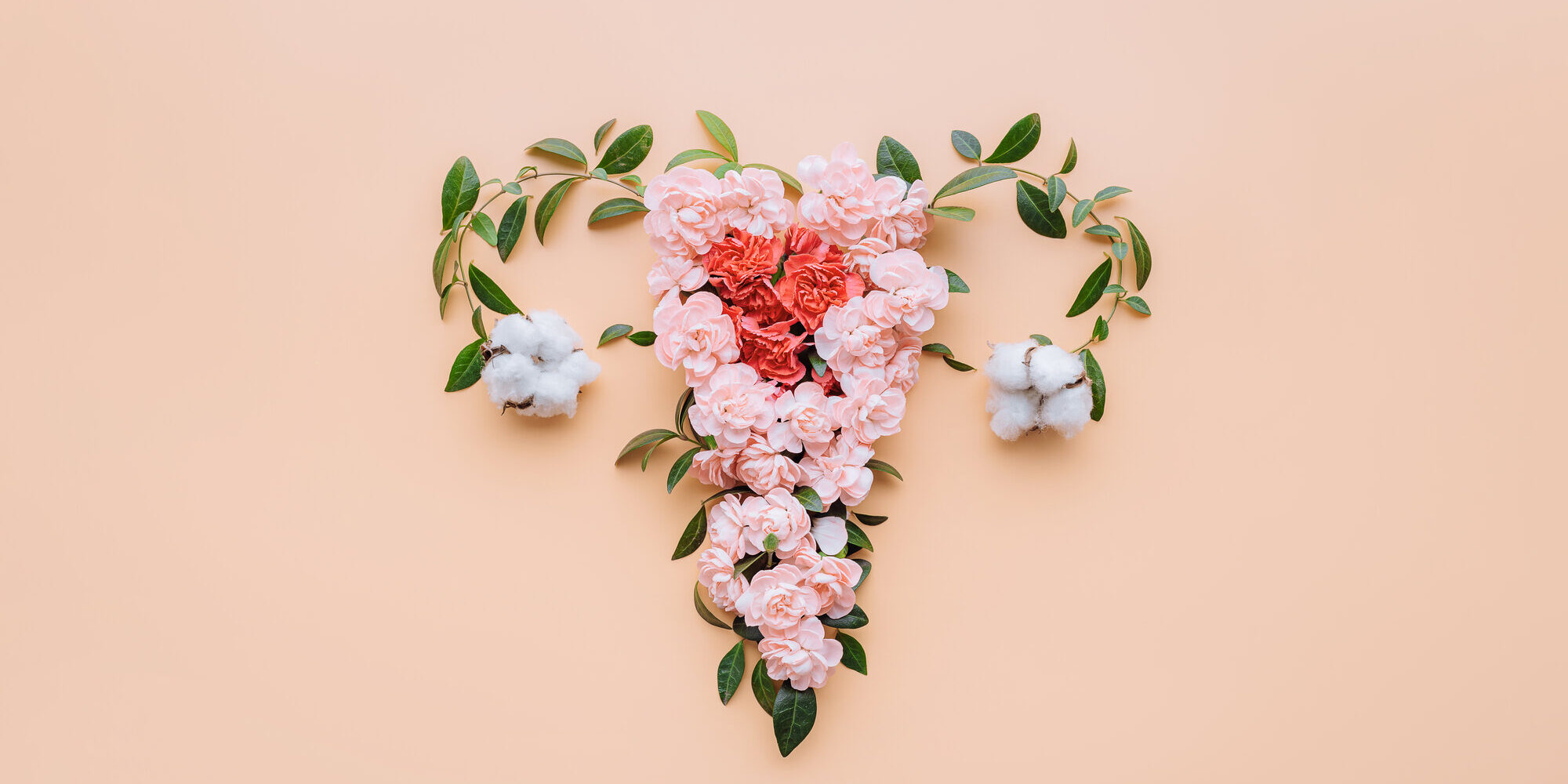 Ein florales Arrangement in Herzform aus rosa Blumen und Baumwollblüten auf einem pfirsichfarbenen Hintergrund.